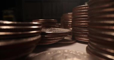 Bakır paralar, masanın üstüne istiflendiğinde kuleler oluşturur. Küçük sikkeler karanlık odada az ışıklandırılmış ihtişam atmosferi taşır.