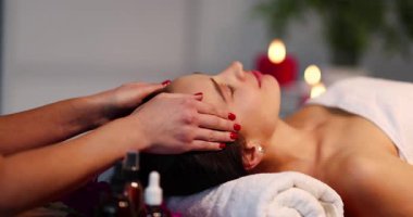 Kozmetik uzmanı genç bir kadının yüzüne masaj yapıyor besleyici yağlar kullanarak sakinlik hissi yaratıyor. Spa ışığı odaya girer. Huzurlu ruh halini ağırdan alır.