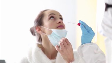 Tıbbi maskeli bir kadın burun temizleme testinden geçiriliyor. Kapsamlı test süreci sağlık taraması ve tanı prosedürü öneriyor