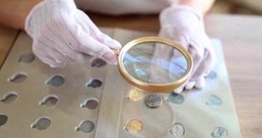 Eldivenli nümismatist, antika paraları dikkatle büyüteçle inceliyor. Koleksiyoncu ayrıntıları ve nadirliği aramak için yüzeyi yakından inceler