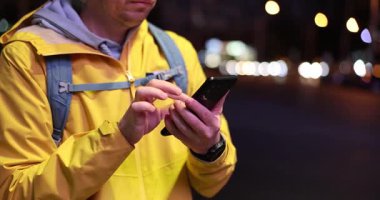 Şehirdeki erkek turist sabit dururken akıllı telefona göz atıyor. Kol saatine bakan kişi, gece saatlerini ve saatlerini onaylıyor.