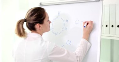 Dişi kimyager beyaz tahta üzerine işaretleyici kullanarak moleküler formül çizer. Parlak oda akademik ruh halinin sınıftaki bilimsel içeriğe odaklanmasını destekler