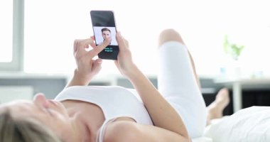 Rahatlamış kadın, yatağa uzanmış randevu uygulamasında romantik bir eş arıyor. Kadın internette erkek fotoğraflarına bakıyor ve akıllı telefondan erkek arkadaşını seçiyor.