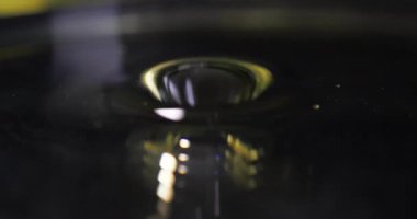 Koyu koyu renkli sıvı, parlak yüzeyine damlayarak eş merkezli dalgalar oluşturur. Damla sıvıya çarpar. Hipnotik görsel ritim makrosu ile dalgalanmalar yayar.