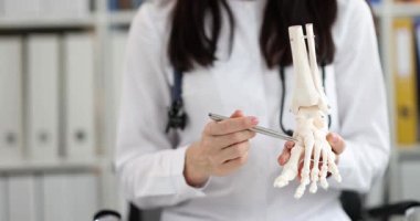 Kadın doktor, insan ayak bileği eklem modelini muayenehanede kalemle gösteriyor. Kadın doktor, klinikte yaralanma nedenlerini ve tedaviyi açıklıyor