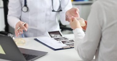 Doktor estetik kliniğindeki kadın hastaya meme implantı örneği veriyor. Plastik cerrah, hastanede ağır çekimde ameliyat öncesi kadınlara danışmanlık yapıyor.