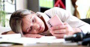 Laboratuvar önlüklü bitkin kadın pembe akıllı telefonu tutarken başını masanın üzerine koyuyor. Klinikte tıbbî deneyimler bitti.