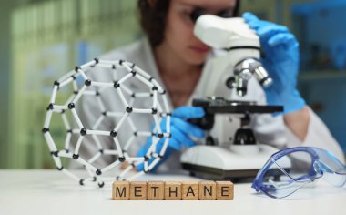 Bir araştırmacı, detaylı bir 3 boyutlu moleküler modelin yanında mikroskop kullanarak metanı yakından inceliyor.