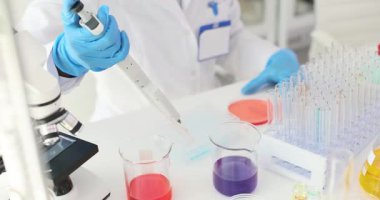 Eldivenli bilim adamı deney tüpü rafı ve mikroskop yakınındaki deney tüpleri arasında sıvı transferi için pipet kullanıyor. Kesin bilimsel deneyler hissi.