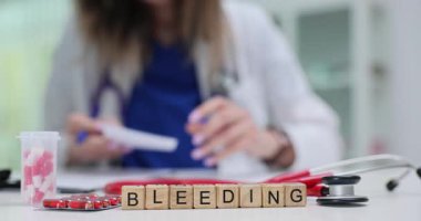 Kan örneği ve kırmızı kapsüllerin yanına konulan tahta küplerden yapılmış bir kelime kanaması. Koyu kırmızı gölgeler ve aletler kanamaya tıbbi tepkiyi yansıtıyor