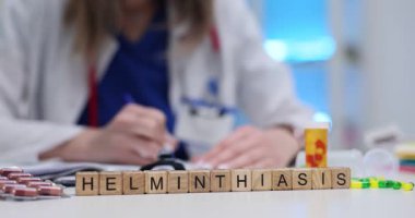 Tahta bloklar Helminthiasis 'i heceleyerek dikkatleri tıbbi açıklıkla çekiyor. Haplar ve harflerin yanındaki şeyler parazit tedavisinin bulaşıcı özünü yansıtıyor.