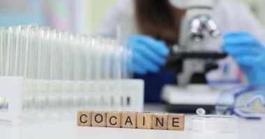 Laboratuvarda mikroskoba bakan teknisyenlerin yanında test tüpleri olan küp üzerinde kelime Kokaini. Sıhhiye, masasında uyuşturucu araştırması yürüten maddeyi analiz ediyor