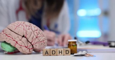 ADHD kısaltması, beyin modeli ve kadın doktor masasında su toplayan haplar. Zihinsel sağlık bozukluğunun nörolojik yönleri ve ilaç seçenekleri