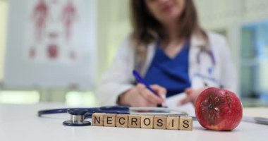 Doktora karşı çürük elma ve steteskopla ahşap bloklardan yapılmış kelime nekrozu. Tıbbi uzman hastanede yatan hastaya reçete yazıyor.