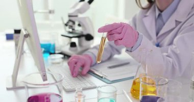 Genç kadın bilim adamı laboratuarda bilgisayar üzerinde çalışan sarı sıvıyla test tüpü tutuyor. Kadın kimyager renk sıvısını dijital teknolojiyle analiz ediyor.