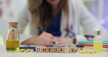 Tahta harfler Omega 9 yazıyor yağ şişesi ve kapsüllerin yanında. Beslenme uzmanı kalp ve kolesterol seviyelerini destekleyen sağlıklı yağ reçetesi yazıyor.