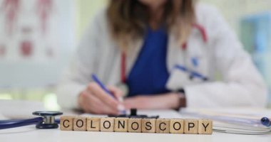 Tahta bloklar, kolonoskopi sözcüğünün steteskop yakınında doktor masasında durduğunu gösteriyor. Gastroenterolog, hastanın bağırsak muayenesine hazırlandığını belirten bir not yazıyor.