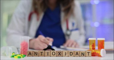 Tahta harfler antioksidan kelimesinin renkli kapsüllerin yanında durmasını sağlar. Sağlık uzmanı hücre savunması için reçeteli ilave yazıyor