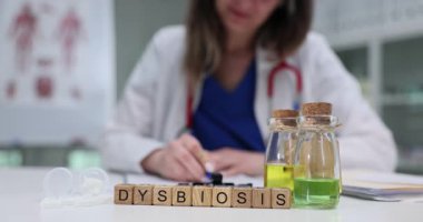 Tahta küpler yeşil sıvı mataraların yanına yerleştirilmiş kelime disbiyozu yaratır. Kadın laboratuvar örnekleri kullanarak bağırsak dengesizliğini analiz eden notlar yazıyor.