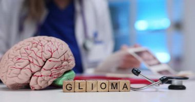 Küpler Glioma kelimesinin ayrıntılı beyin modeli ve steteskopun yanında durduğunu söyler. Sinir ve tarama kağıtları tümör değerlendirmesi ve nörolojik odak