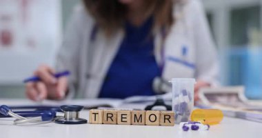 Tahta bloklar, dağınık kapsüllerin ve görüntülerin yanına yerleştirilmiş Tremor sözcüğünü heceler. Nörolojik taramalar ve sallanan ilaç şişesi motor semptomları yansıtıyor