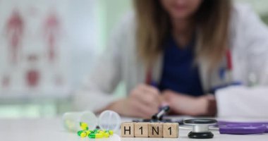 Palto giyen doktor masasında H1N1 harfleriyle çalışıyor. Sarı ve yeşil kapsüllerdeki haplar bulaşıcı hastalıklara ve tedaviye odaklandığını gösteriyor.