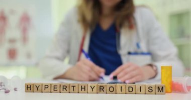 Profesyonel bir kadın, masasında hipertiroidizm olan kağıtlarla çalışıyor. İlaç şişeleri tiroid durumlarına ve tedaviye odaklandığını gösteriyor.