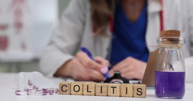 Laboratuvar önlüklü kadın, tahta blokların yanında Colitis 'li bir belge yazıyor. Mor sıvı ve haplarla dolu şişe gastrointestinal sağlığa odaklandığını gösteriyor.