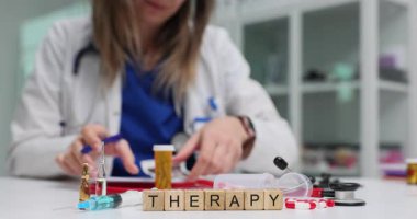 Laboratuvar önlüklü profesyonel, terapi masasında çalışıyor. Yanında da birkaç blok ötede belgeler var. Ampuller şırıngalar ve ilaç şişeleri tedaviye odaklanmamızı öneriyor