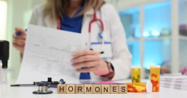 Masasında tahta kiremitler üzerinde hormonlar yazan kadın profesyonel analiz belgesi. İlaç şişeleri tartışmayı ve endokrin sağlığına odaklanmayı önerir