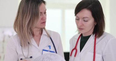 Ciddi kadın doktorlar hastane tıbbi kayıtlarını yavaş çekimde tartışıyor. Kadın doktorlar tedavi planını onaylıyor Klinikteki belgeleri kontrol ediyorlar