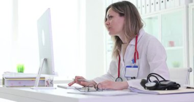 Kadın doktor hastane ofisindeki bilgisayar kontrolünde çalışıyor. Kadın tıp uzmanı klinikteki işyerindeki internet tıbbi kayıtlarını dolduruyor.
