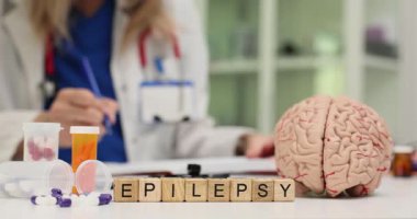 Kadın, tahta blokların yakınındaki kağıtlara insan beyni modelinin yanındaki masada epilepsi ile yazı yazıyor. Nörolojik durum ve hasta tedavisine odaklanın