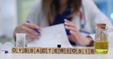 Sarı sıvı şişe disbacteriosis kelimesinin yanında duruyor. Laboratuvar ışığını yakalayan bloklardan yapılmış. Kadın bağırsak flora dengesizliği üzerine çalışan bir kağıt tutuyor.