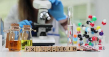Psilosibin kelimesi, laboratuvar ışığı altında molekül modelinin yanına konan bloklardan oluşur. Bilim adamı mikroskop kullanarak psikedelik bileşik etkilerini araştırıyor.