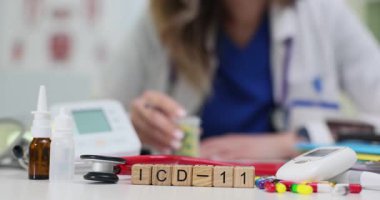 Tahta bloklardan oluşan ICD-11 dijital cihazlar ve burun spreyinin yanında duruyor. Doktor, tedavi için ilaç seçmek için tıbbi tablolarla çalışıyor.