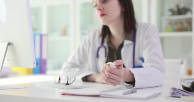 Kadın doktor masasında oturmuş, düşünceli bir ifadeyle stres topunu sıkıyor. Tıp mesleğindeki stres, sağlık hizmetlerinin doğasını gerektiren önemli noktalar