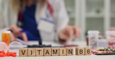 Tahta küplerde doktor masa başında çalışırken B6 vitamini takviyeleri destekliyor. İlaç paketleri vitaminlerin önemini gösteriyor.