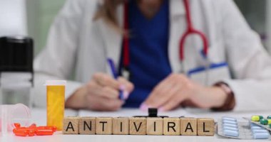 Tahta bloklar, doktor reçetesi yazarken antiviral tedaviyi açıklıyor. İlaç paketleri yakınlarda ilaç ve sağlık kontrollerini gösteriyor.