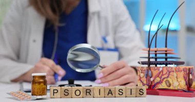 Tahta bloklar sedef hastalığını gösterirken doktor büyüteçle çalışıyor. Deri katmanı modeli ve haplar delikanlı masasının üstünde duruyor.