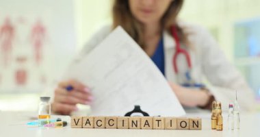 Tahta bloklar, doktorların gazete okuduğu yerlerde sağlık güvenliğini destekleyen kelime aşısı oluşturur. Şırınga şişeleri ve steteskop küplerin yanındaki masada.