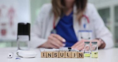 Tahta bloklar hormon önemini yansıtan insülin kelimelerini oluşturur. Doktor damgasıyla klinik içeriği gösteren cam bardaklar masanın üzerinde duruyor.