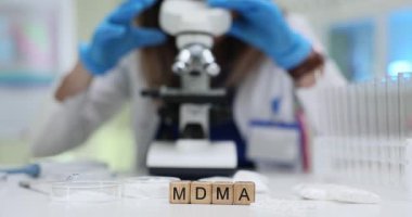 Masasında ekstazi ve mavi eldivenli bilim adamı olan tahta bloklar mikroskopla test tüplerinin yakınına bakıyor. Laboratuvarda adli tıp ve uyuşturucu analizi