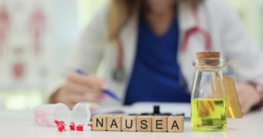 Ahşap bloklarda mide bulantısı, masada bir şişe sıvı ve çalışan bir doktorla. Mide bulantısı tedavisi klinikte ilaç ve bitkisel tedaviyi kapsar