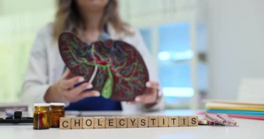 Küpler, anatomik karaciğer modelinin yanındaki kolesistit 'i doktorun ellerinde heceliyor. Kelime, safra kesesi iltihabını açıklayan organ fonksiyonuyla doğrudan ilişkilidir.