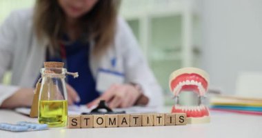 Ağız modelinin yanına yerleştirilmiş küplerde ve sarı sıvıda kelime Stomatiti görülüyor. Diş terimi çene modeline bağlanır ve oral sorunu önleyen sıvılar