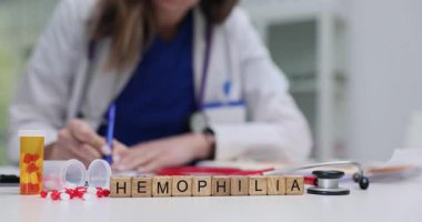 Scrabble küpleri hemofili 'yi test tüplerinin yanında ve ilaç kutuları kanama bozukluğu olduğunu gösteriyor. Yumuşak ışık odaya girer, doktor yazmakla meşgul olduğunu gösterir.
