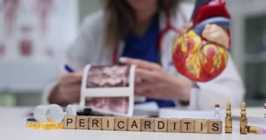 Kalp modelinin yanındaki bloklarda kelime perikarditi görülüyor ve kardiyoloji temasını yansıtan organ diyagramı. Gün ışığı uzaya girer ve sakin bir atmosfer yaratır.