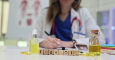 Tahta bloklar, balık yağının cam şişelerin ve sarı kapsüllerin yanında durduğunu gösteriyor. Sıcak ışık, doktorların not yazarken etrafını sükunetle dolduruyor.