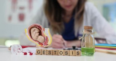 Tahta küplerden yapılan jeoz kelimesi rahim modelinde hamilelikle ilgili riskleri sembolize eder. Blokların arkasında doktor notlar alır ve olay çıkartır.